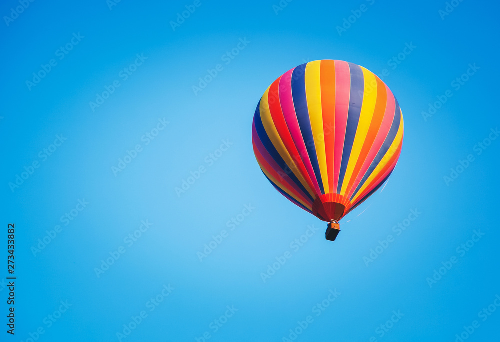 Fototapeta premium Bright striped multicolored balloon in the blue sky, freedom of travel adventure