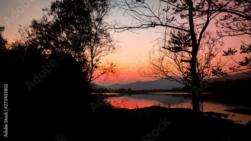 Landscape with orange and purple at sunset silhouettes of mountains, hills and forest lake
