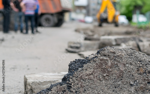 a piece of asphalt on the destroyed road yard of a house on the background of construction equipment, truck, tractor, excavator and working people