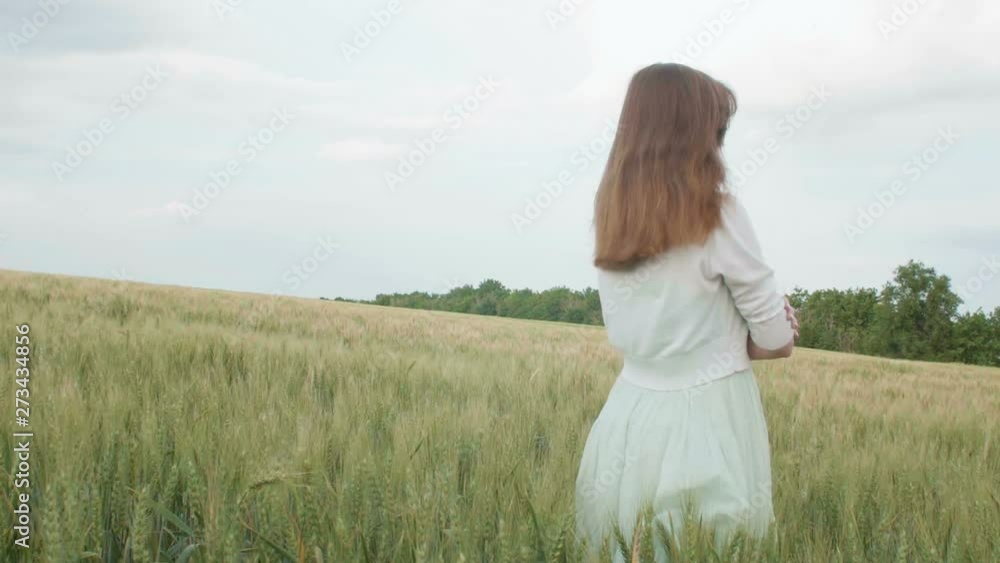 Beautiful young russian girl among the tall green spikelets of wheat in the field. Young woman enjoying summer, harmony of human and nature, health and solitude Beautiful young russian girl among the tall green spikelets of wheat in the field. Young woman enjoying summer, harmony of human and nature, health and solitude