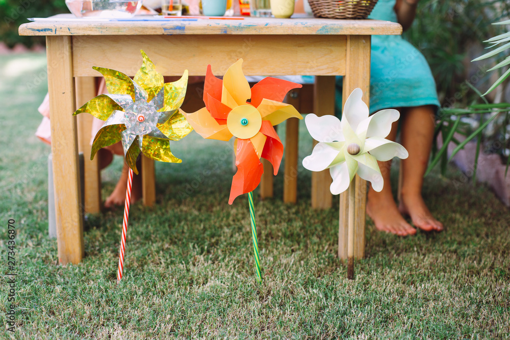 Fototapeta premium Three colorful toy windmills in the grass with kids feet on the background