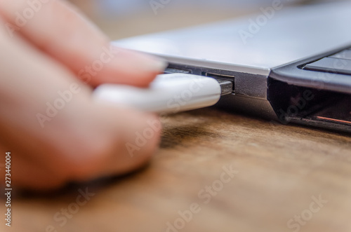 Closeup of woman s hand plugging white USB flash drive into laptop on a wooden table