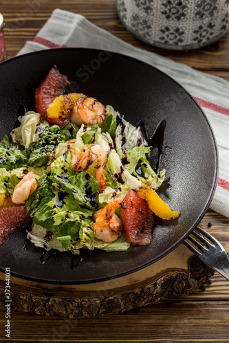 shrimp salad with sliced grapefruit, orange and lettuce on brown plate on wooden table