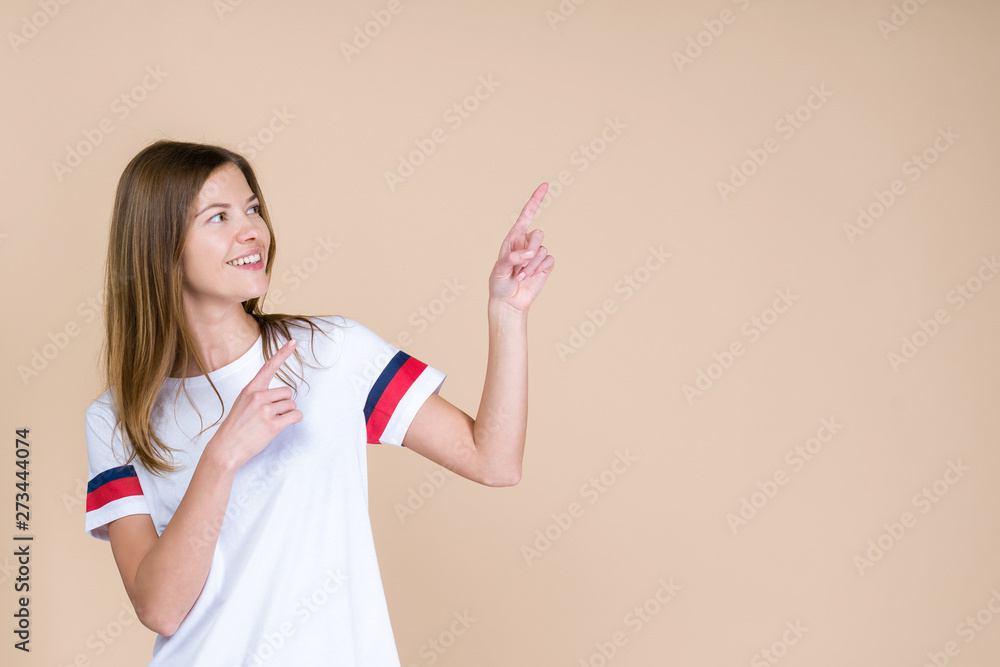 Young woman with smile pointing fingers away, standing on pastel beige background Young woman with smile pointing fingers away, standing on pastel beige background