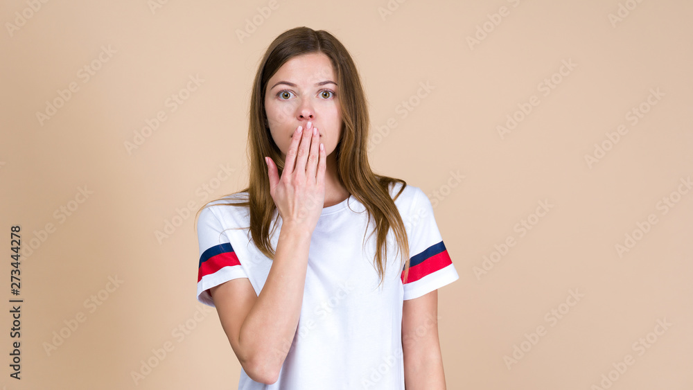Young worried woman standing on pastel beige background and holding palm hand near face Young worried woman standing on pastel beige background and holding palm hand near face