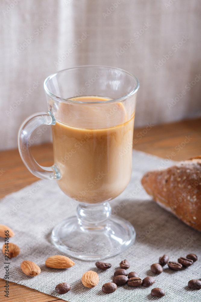 Glass cup of coffee with cream and bun on a wooden background and linen textile. Glass cup of coffee with cream and bun on a wooden background and linen textile.