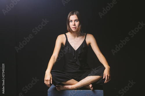 Young Caucasian female model posing in studio black background.Girl sitting in a black dress on a dark wall. Subject severe poor psychological state, intra, problems, personality conflict