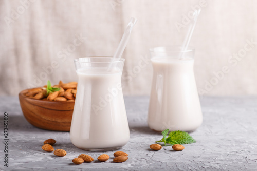 Organic non dairy almond milk in glass and wooden plate with almond nuts on a gray concrete background.