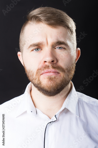 Close up portrait of handsome serious bearded man standing against black wall
