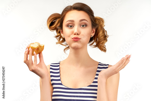 A happy girl in a striped t-shirt holds a donut in her hand and chews a donut with her mouth full. Funny cute expression of a young sweet tooth. The concept of a quick and tasty snack