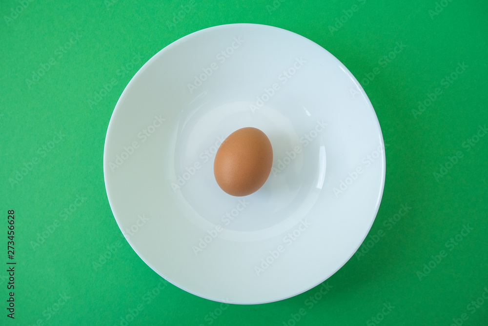 brown raw egg in white plate on green background brown raw egg in white plate on green background