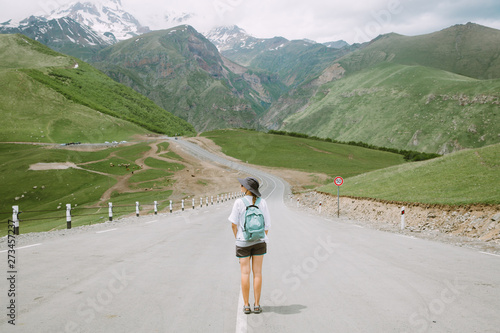 Young woman tourist standing in the middle of the road leading to the Georgian mountains