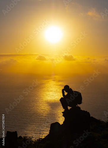 Silhouette of man on top sitting meditating at sunset with sun over sea.
