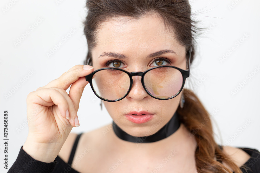 Closeup portrait of a beautiful young woman in black clothes with a ribbon on her neck holding glasses posing on a white background. Concept of a smart young female student or businesswoman