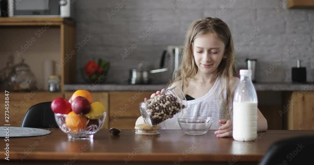 Beautiful schoolgirl pouring milk into a bowl of cornflakes in the kitchen. Beautiful schoolgirl pouring milk into a bowl of cornflakes in the kitchen.