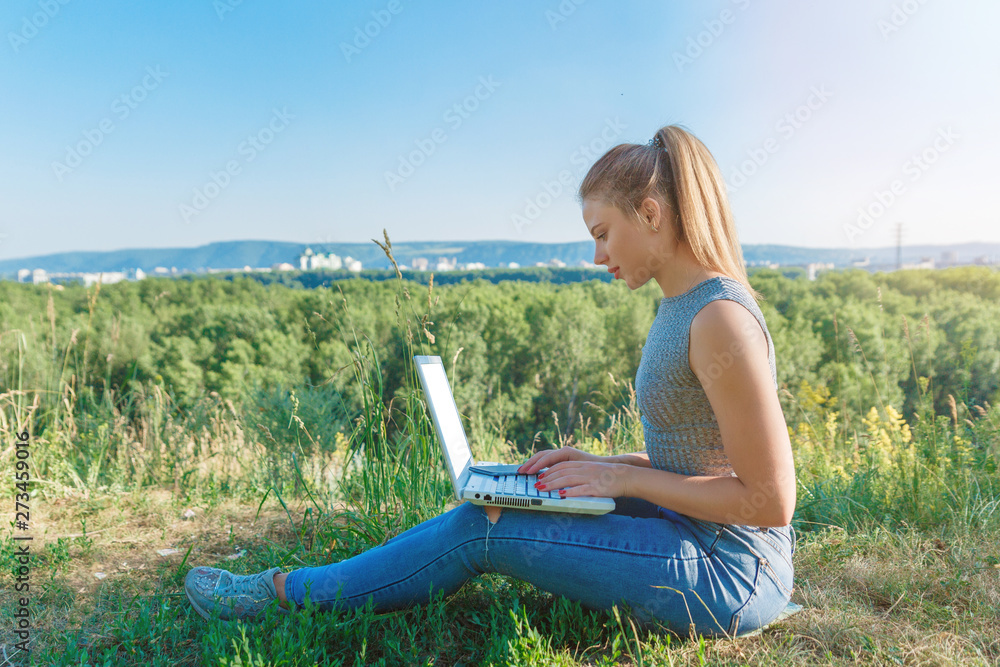 A girl with a laptop in nature, against the forest and the sky with sunlight. The concept of combining leisure and work. Individual entrepreneur. Work at the computer away from the city. A girl with a laptop in nature, against the forest and the sky with sunlight. The concept of combining leisure and work. Individual entrepreneur. Work at the computer away from the city.
