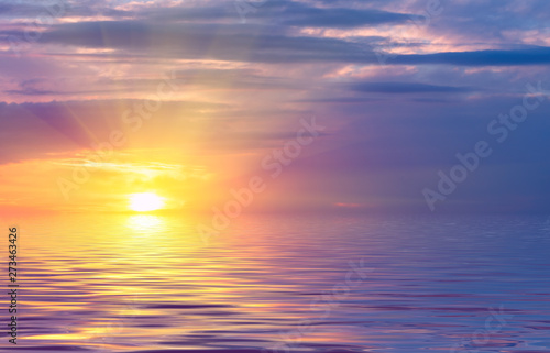 Sunset on the sky, bright sun and colored clouds over the rays against the backdrop of sea waves.