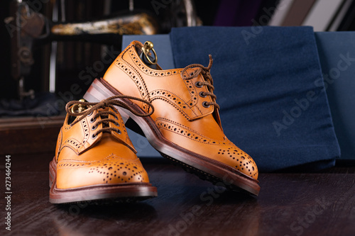 Brown full grain leather brogues on wooden display in in men shoes boutique store with box and cloth shoe bags. photo