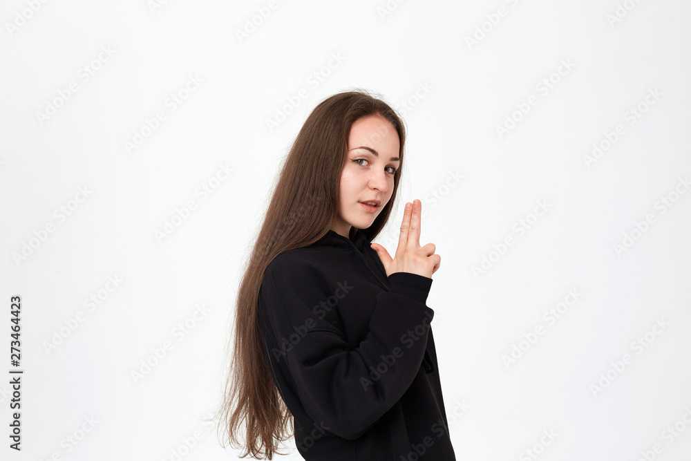 Young pretty brunette woman wears black sweatshirt and stands over white background. Girl holds imaginable gun in her hands. Young pretty brunette woman wears black sweatshirt and stands over white background. Girl holds imaginable gun in her hands.