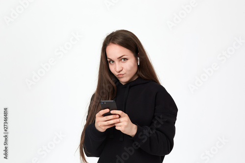 Studio shot of a beautiful young brunette woman with wireless headset and phone looking intrigued at the camera while standing over white background.