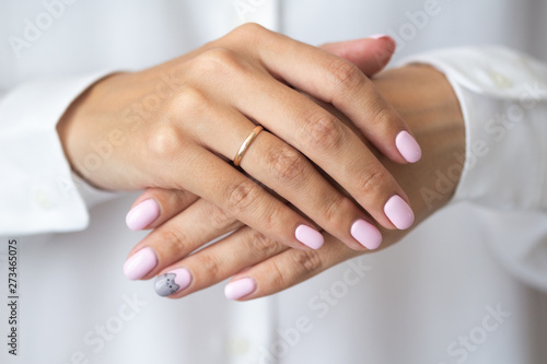 Close-up photo of elegant light pink manicure over white shirt background, tender women's hands with perfect nails, spa and care
