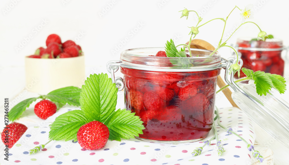 Delicious strawberry jam in traditional glass jar on white wooden background Delicious strawberry jam in traditional glass jar on white wooden background
