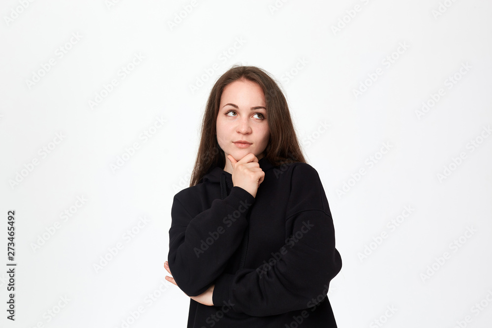 Young beautiful brunette woman looking at the right upper corner with hand raised on chin while standing on a white background. Young beautiful brunette woman looking at the right upper corner with hand raised on chin while standing on a white background.