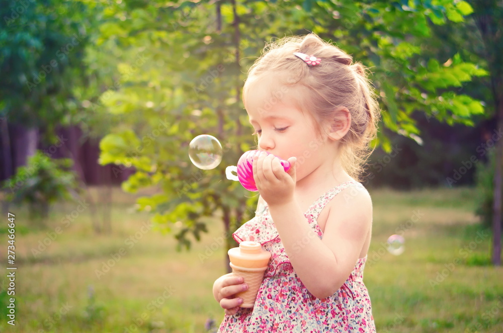 Portrait of little funny girl with soap bubbles in summer in park