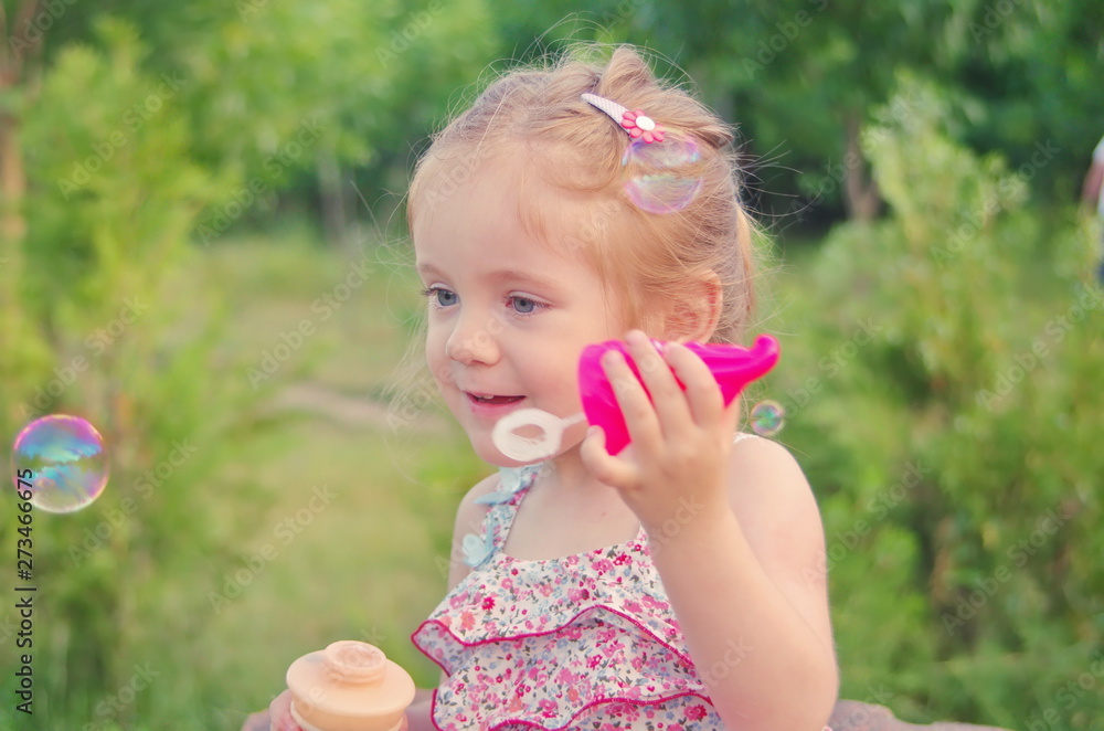 Portrait of little funny girl with soap bubbles in summer in park