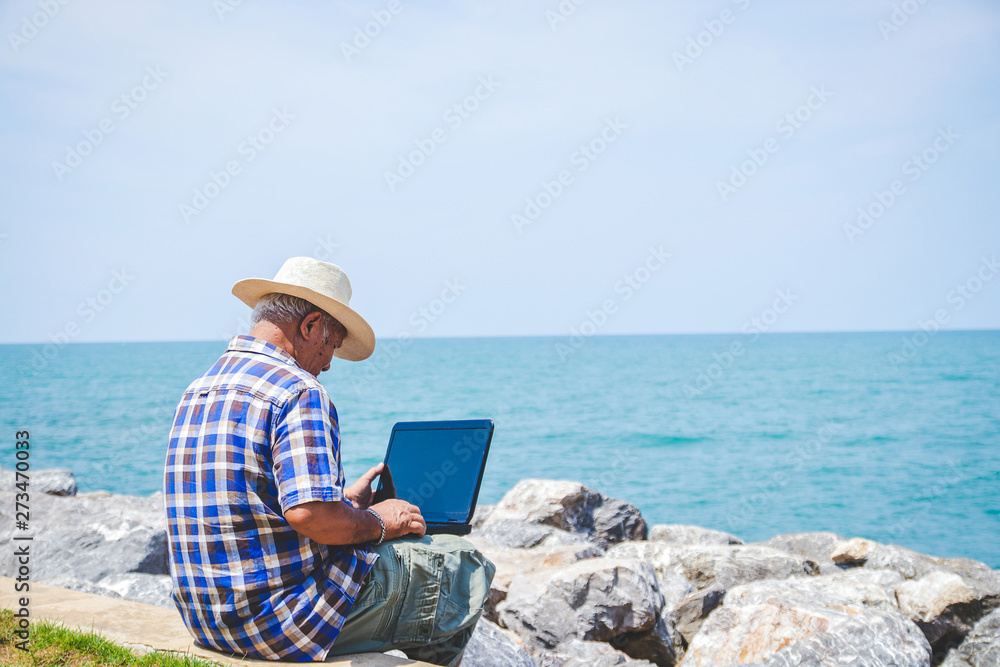 An elderly man carrying a laptop computer sitting at work by the sea