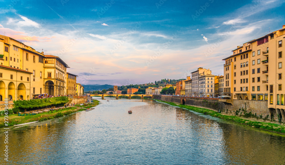 Ponte alle Grazie stone bridge and boat on Arno River water and embankment promenade with buildings in historical centre of Florence city, bright blue orange evening sky clouds, Tuscany, Italy