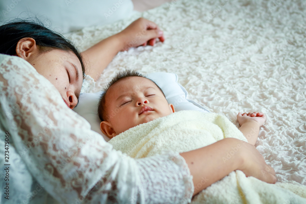 Mom lay hugging a baby son asleep on a white bed. Mom lay hugging a baby son asleep on a white bed.