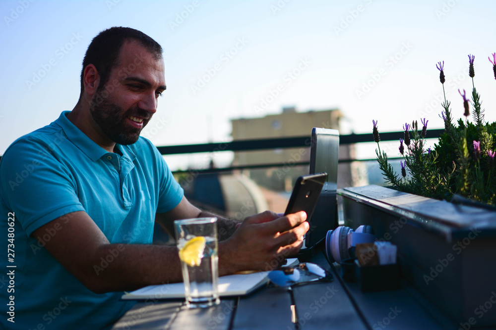 Happy young man browsing internet on smartphone sitting at outdoor cafe. Happy young man browsing internet on smartphone sitting at outdoor cafe.