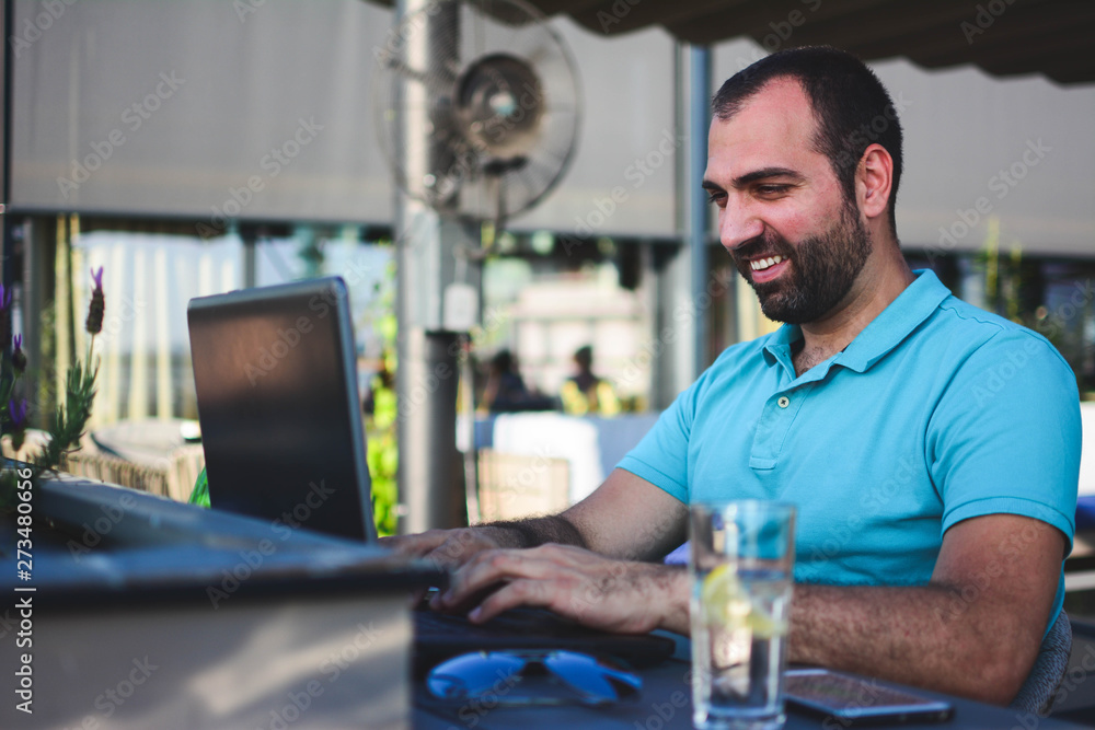 Satisfied with work done. Happy young man working on laptop while sitting at outdoor cafe. Satisfied with work done. Happy young man working on laptop while sitting at outdoor cafe.