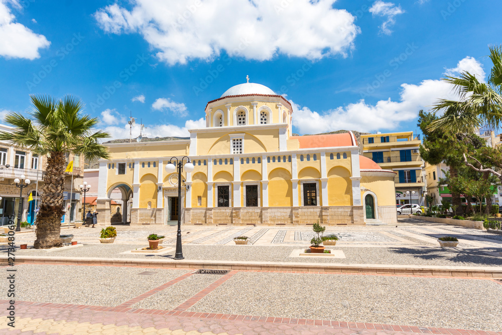 beautiful square in the Kalymnos city with church yellow colour  and black-white pebble mosaic on the floor at sunny day in Greece Kalymnos Island  Dodecanese archipelago