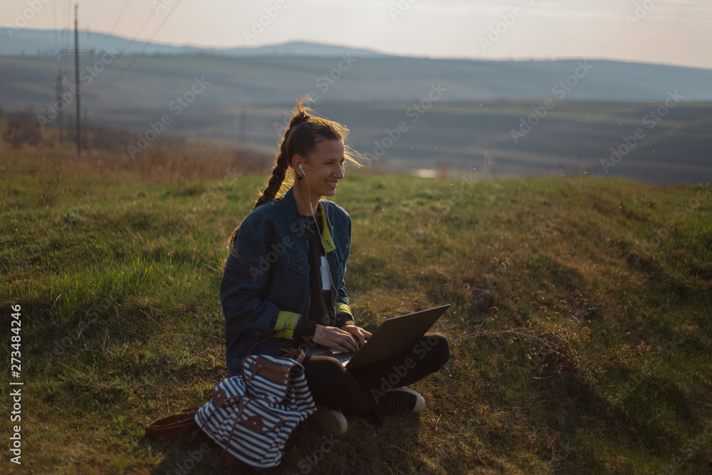 young girl working at laptop with earphones in the fields 