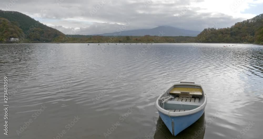Static shot of a lone boat docked on a calm lake with the mountains in the background Static shot of a lone boat docked on a calm lake with the mountains in the background
