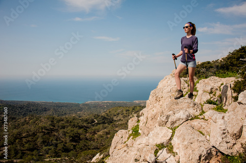 Sporty girl standing on the rock in shorts with walking sticks