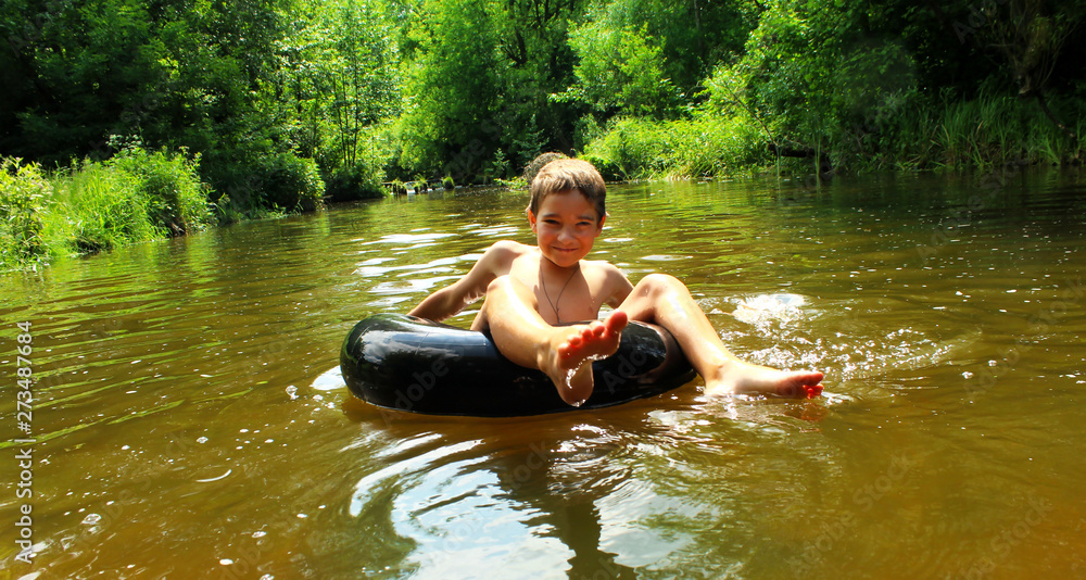 Fototapeta premium The boy has fun on an inflatable tubing in the river.