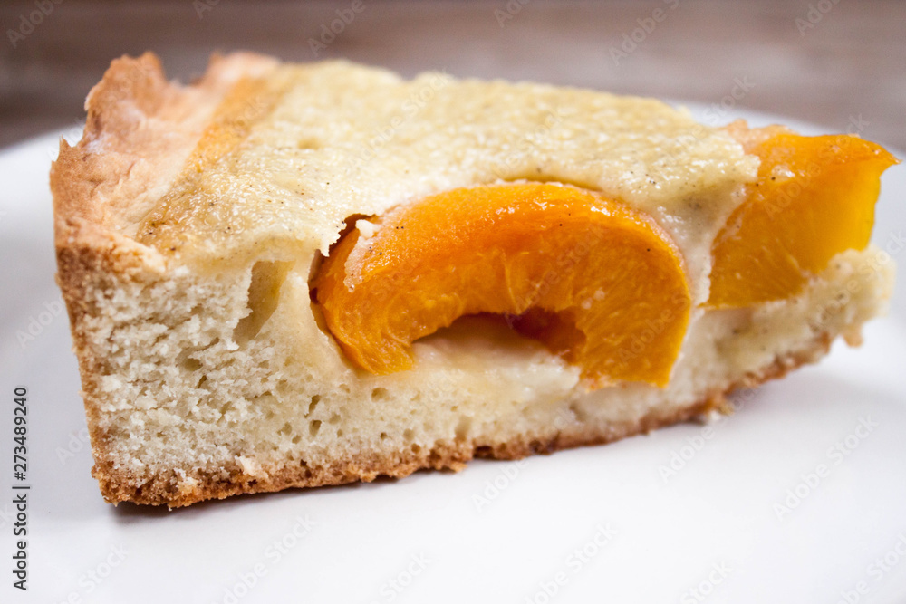 Slice of open peach apricot pie on white plate on wooden table horizontal macro close-up.