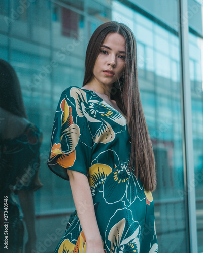 Beautiful girl model posing against the background of the glass building in a wonderful dress.