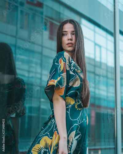 Beautiful girl model posing against the background of the glass building in a wonderful dress.