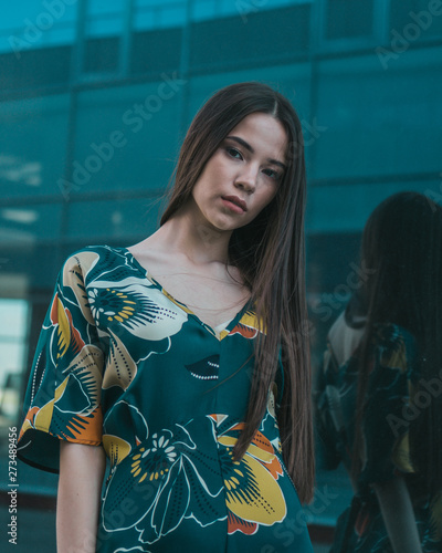 Beautiful girl model posing against the background of the glass building in a wonderful dress.