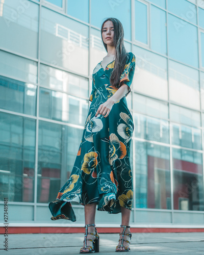 Beautiful girl model posing against the background of the glass building in a wonderful dress.
