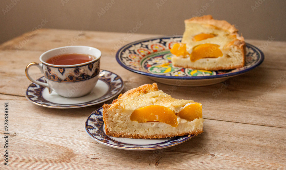 Slice of peach apricot pie or cheese sour cream cake on bright saucer with tea cup on wooden table