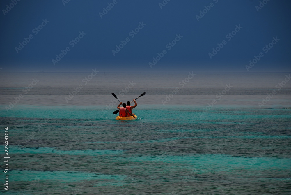 Extraordinary image of two people rowing on a canoe on a sea of wonderful green and blue colors that stands out against a cobalt sky