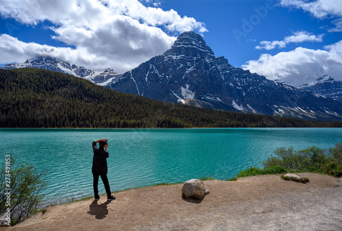 A tourist is amazed by the scenic view of the Bowl Lake with the surrounding mountains and taking photo of it on the Icefields Parkway in Banff National Park