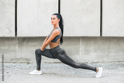 Fitness beautiful woman model in stylish clothes doing stretching muscles exercises on city streets. Sporty fashion girl in leggings trains outdoors. 