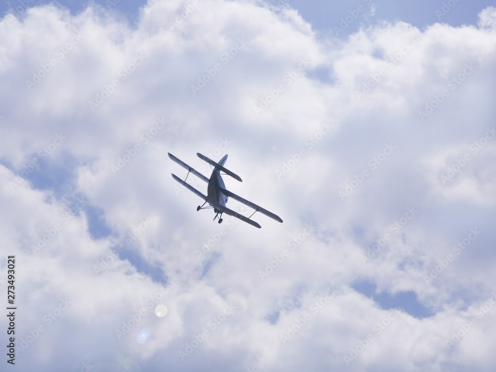 Flying light aircraft blue on a background of white clouds. Bottom view of airplane silhouette Flying light aircraft blue on a background of white clouds. Bottom view of airplane silhouette