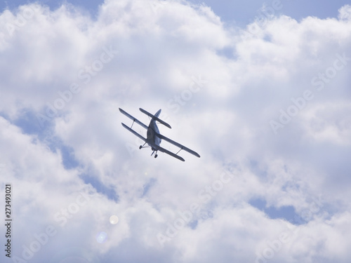 Flying light aircraft blue on a background of white clouds. Bottom view of airplane silhouette